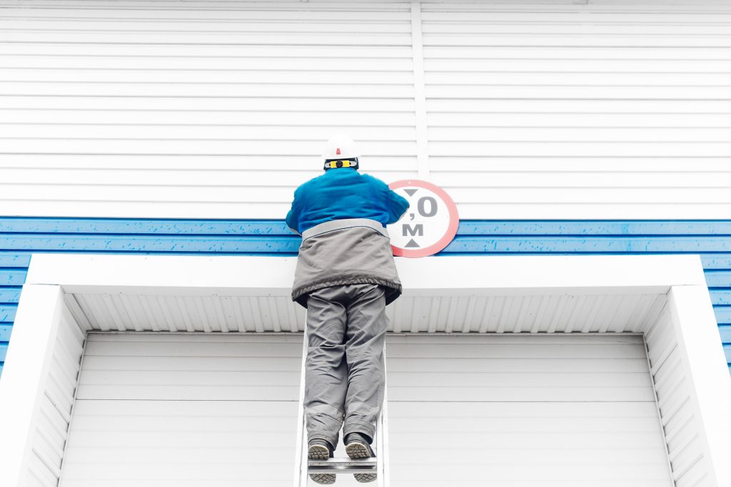 Professional Shutter Repair A worker wearing a hard helmet is cleaning roller shutters. View from behind.